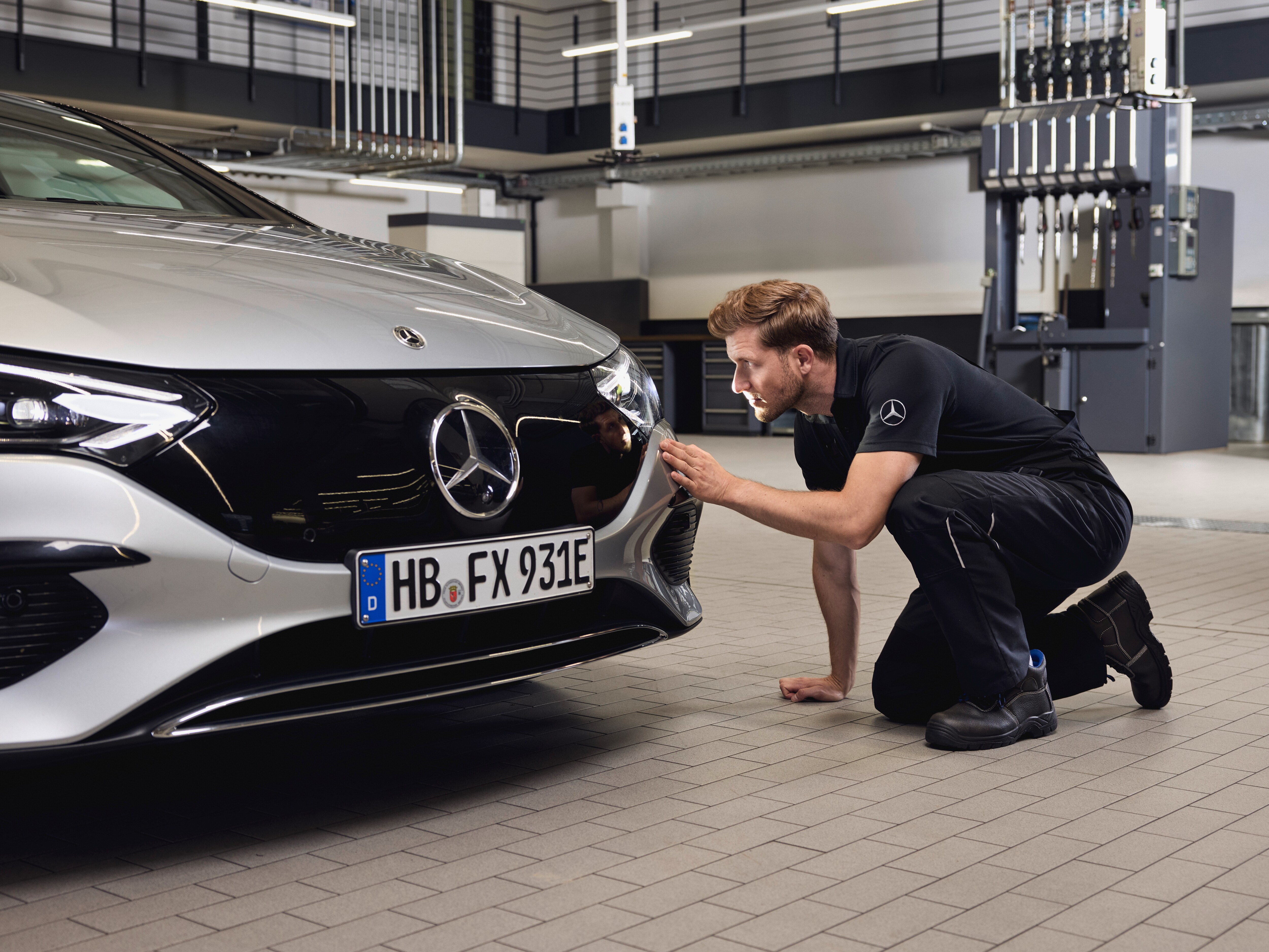 Grande plano da frente de um veículo Mercedes-Benz com um técnico realizando um exame detalhado sobre a substituição de peças genuínas Mercedes-Benz.