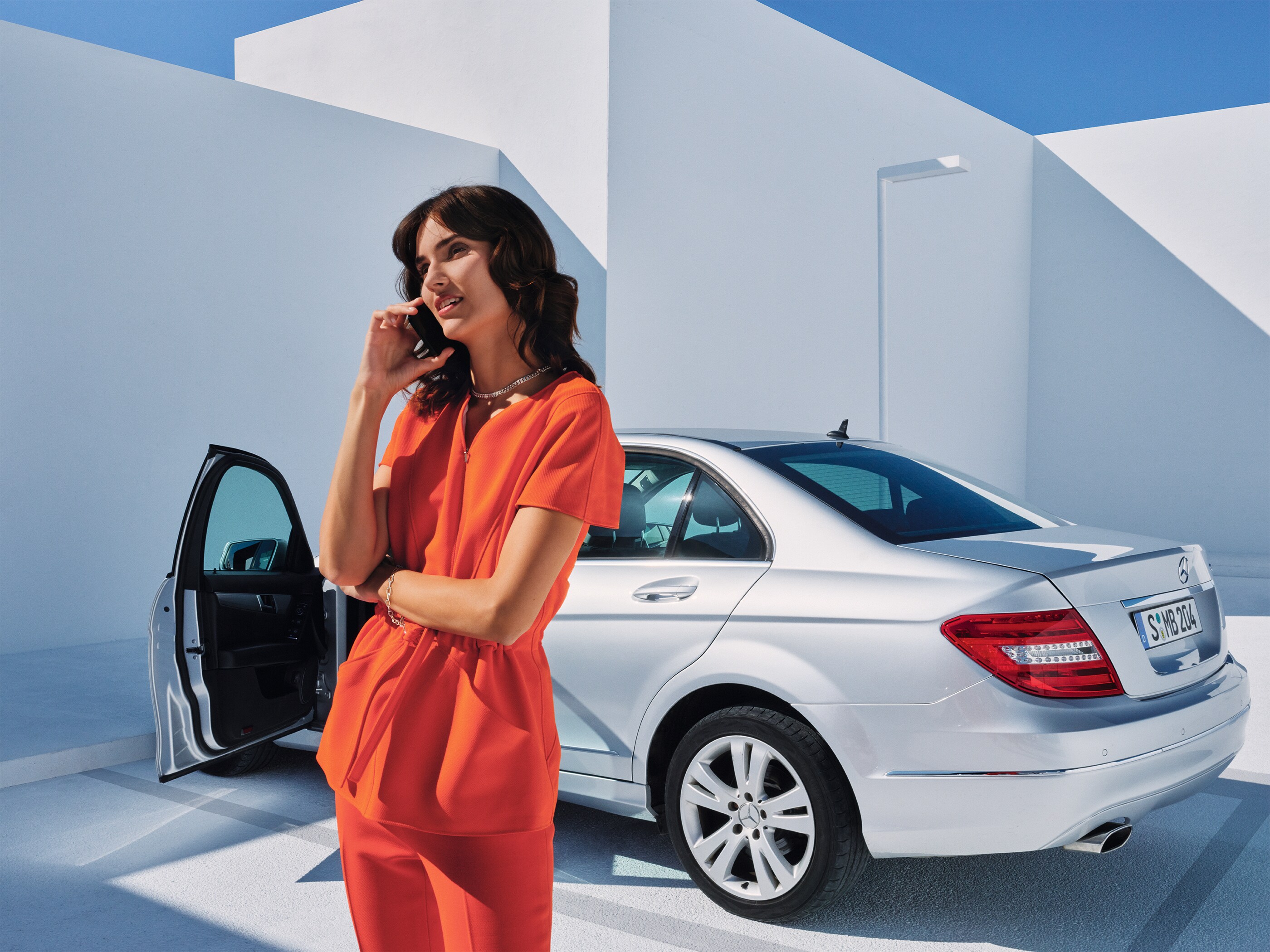 Uma mulher falando ao telefone em frente a um Mercedes-Benz.