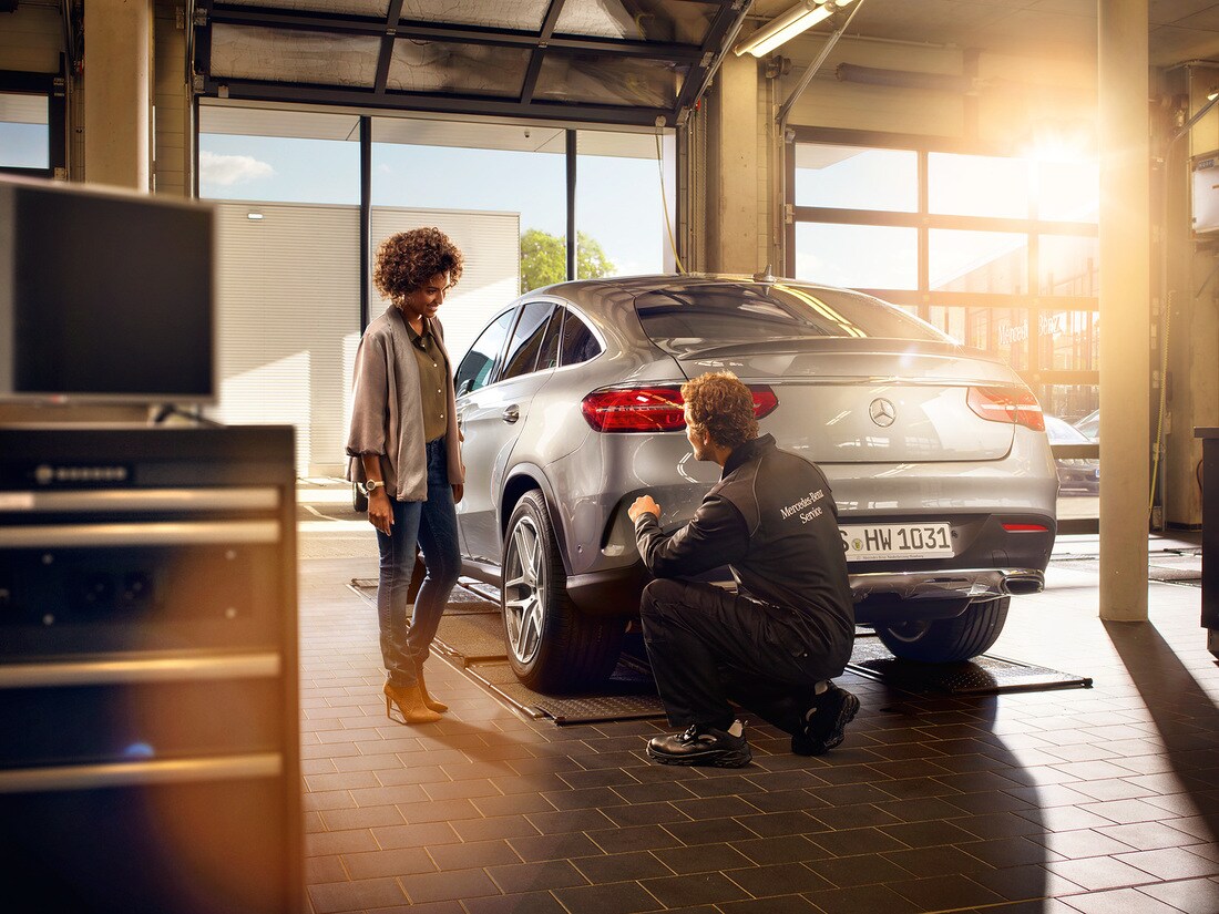 Um técnico Mercedes-Benz se ajoelha na frente de um veículo e realiza a inspeção principal.