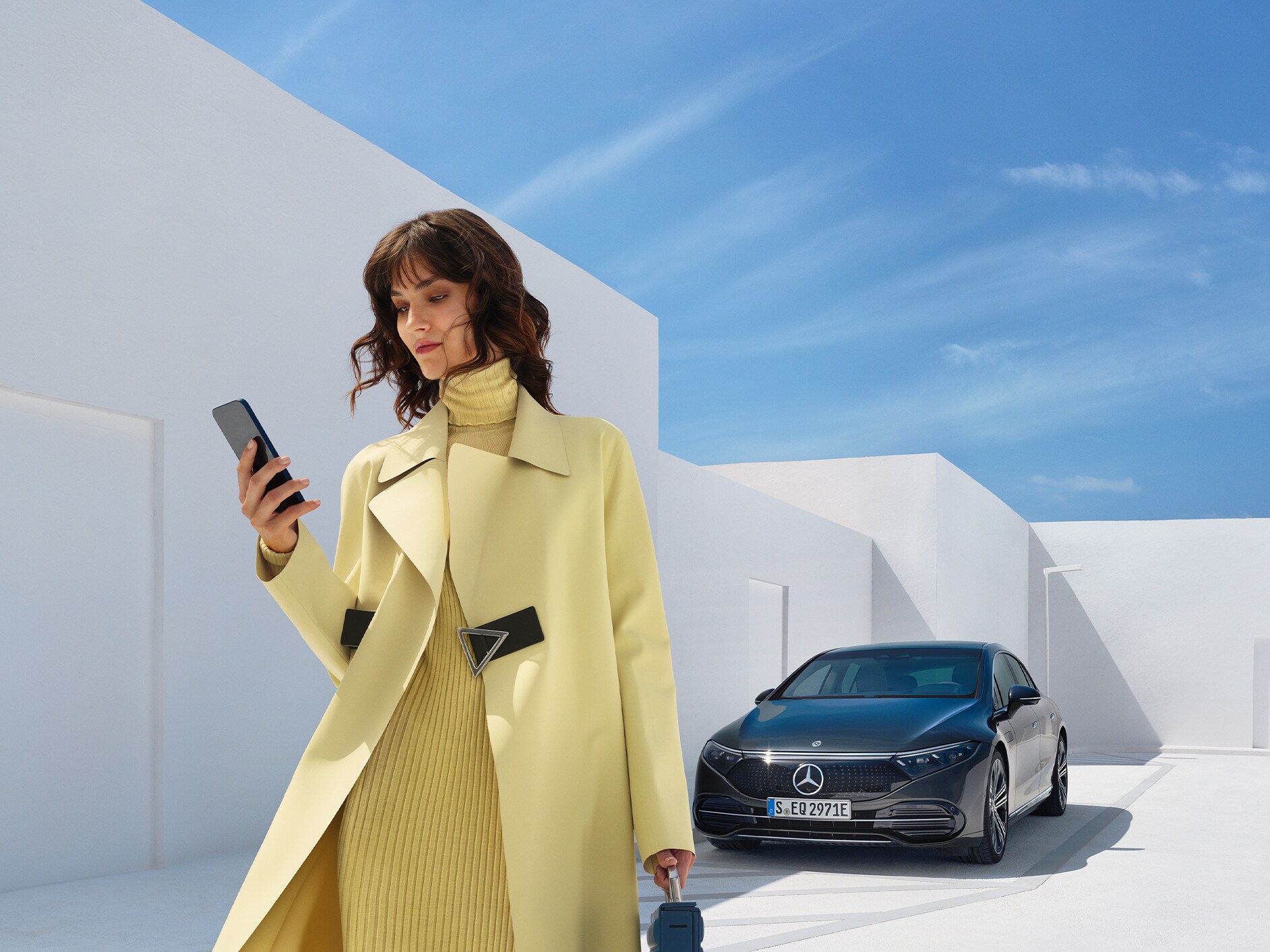 Uma mulher olha para o seu celular enquanto se afasta do seu veículo Mercedes-Benz com tecnologia EQ.