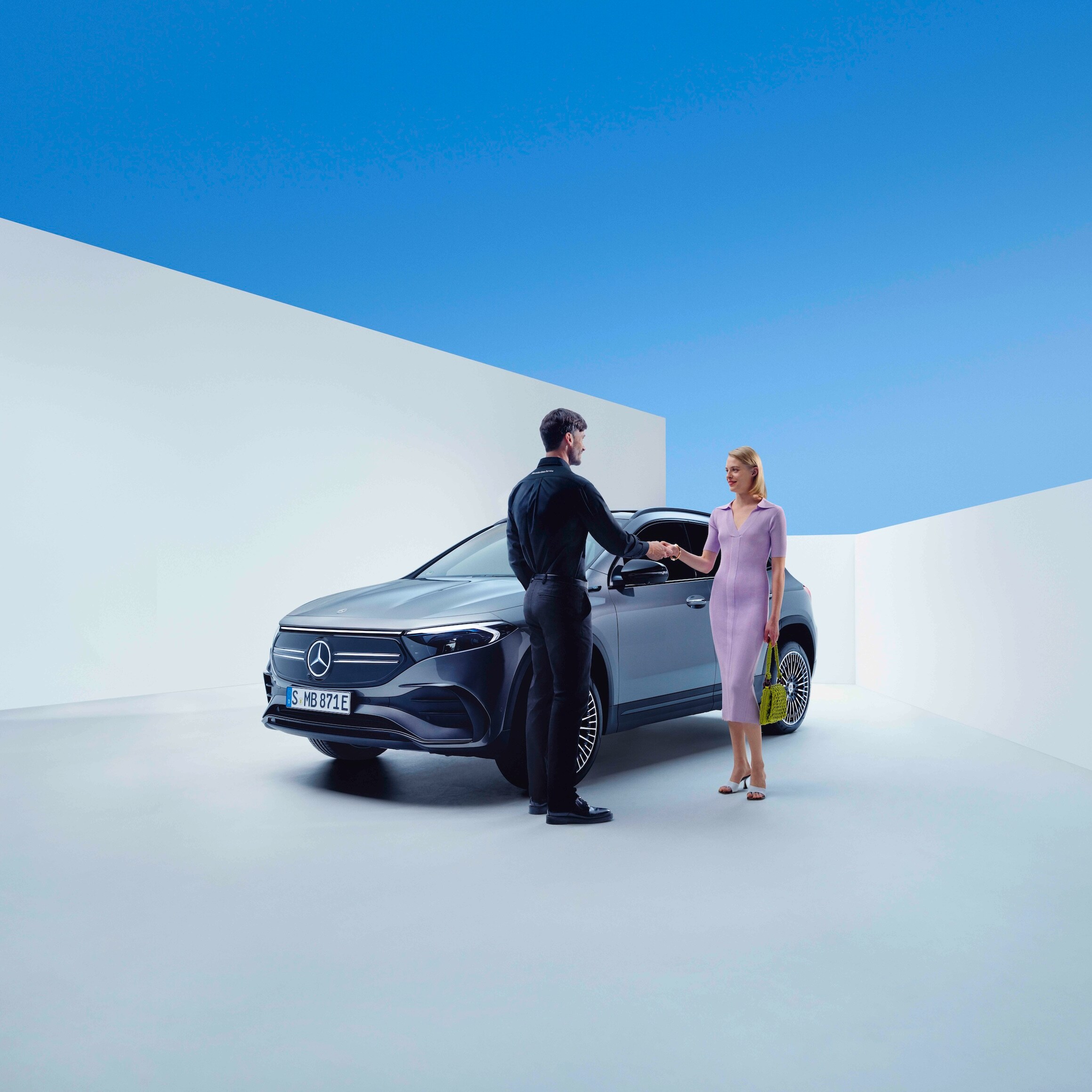 Aperto de mão entre um funcionário da Mercedes-Benz e uma mulher, diante de um Mercedes-Benz
