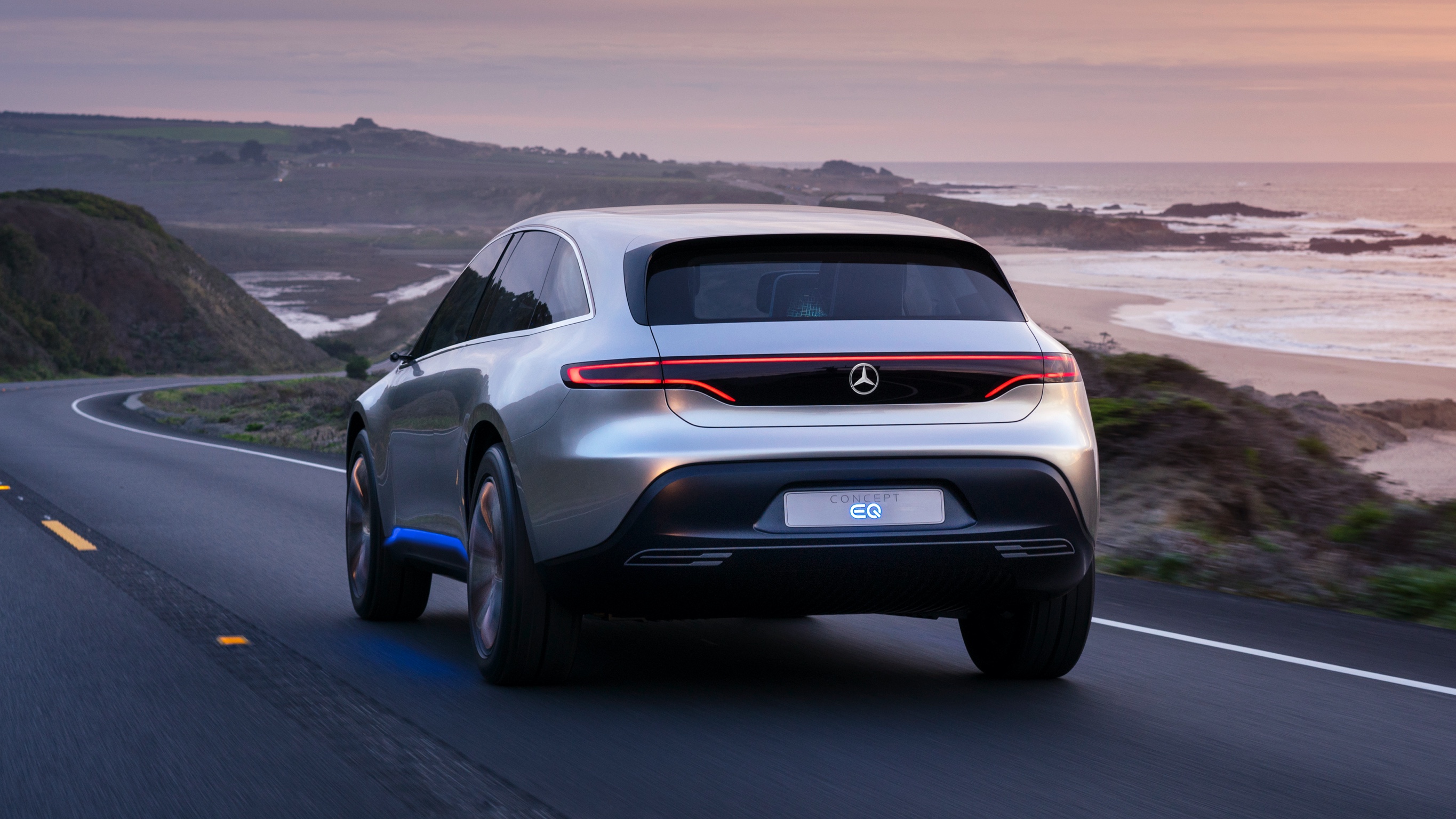 Sustentabilidade Mercedes-Benz: Impulsionado pelo amanhã Um EQ de uma perspectiva traseira em uma estrada costeira.